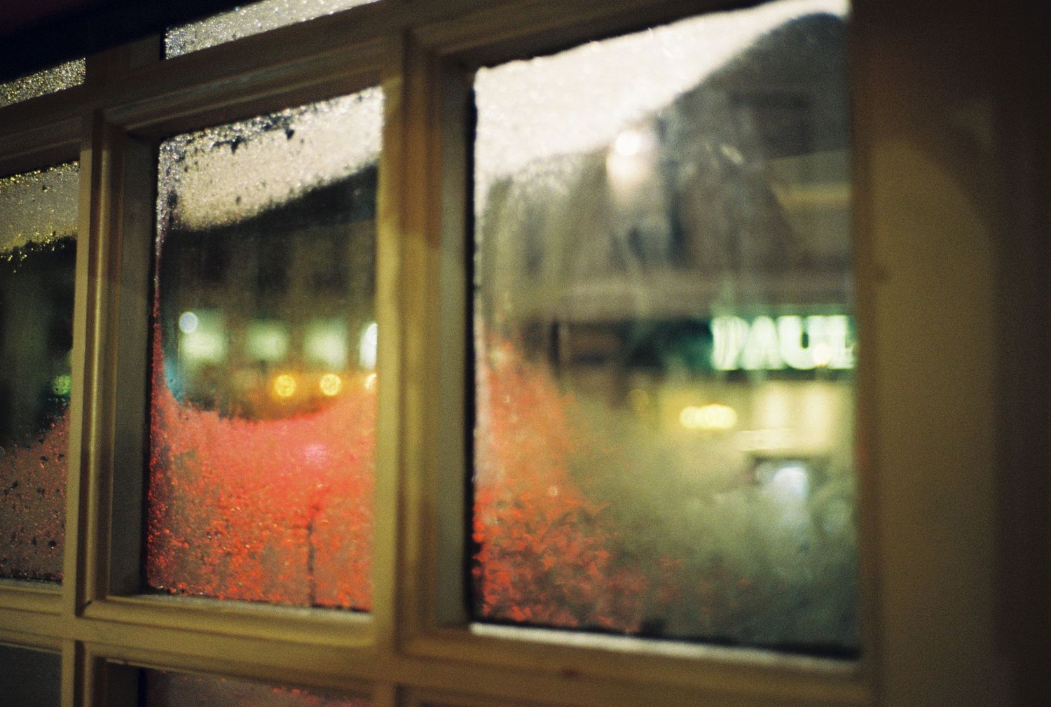 Condensation on a window pane at night with blurred red lights visible in the background.