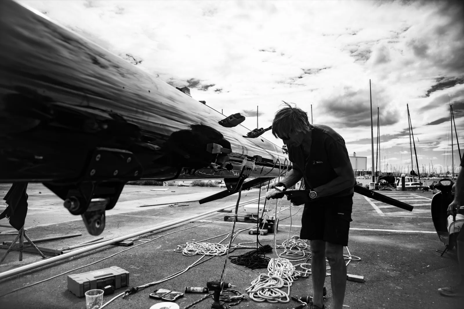 Scène en noir et blanc d’un homme travaillant sur un voilier amarré dans un port.