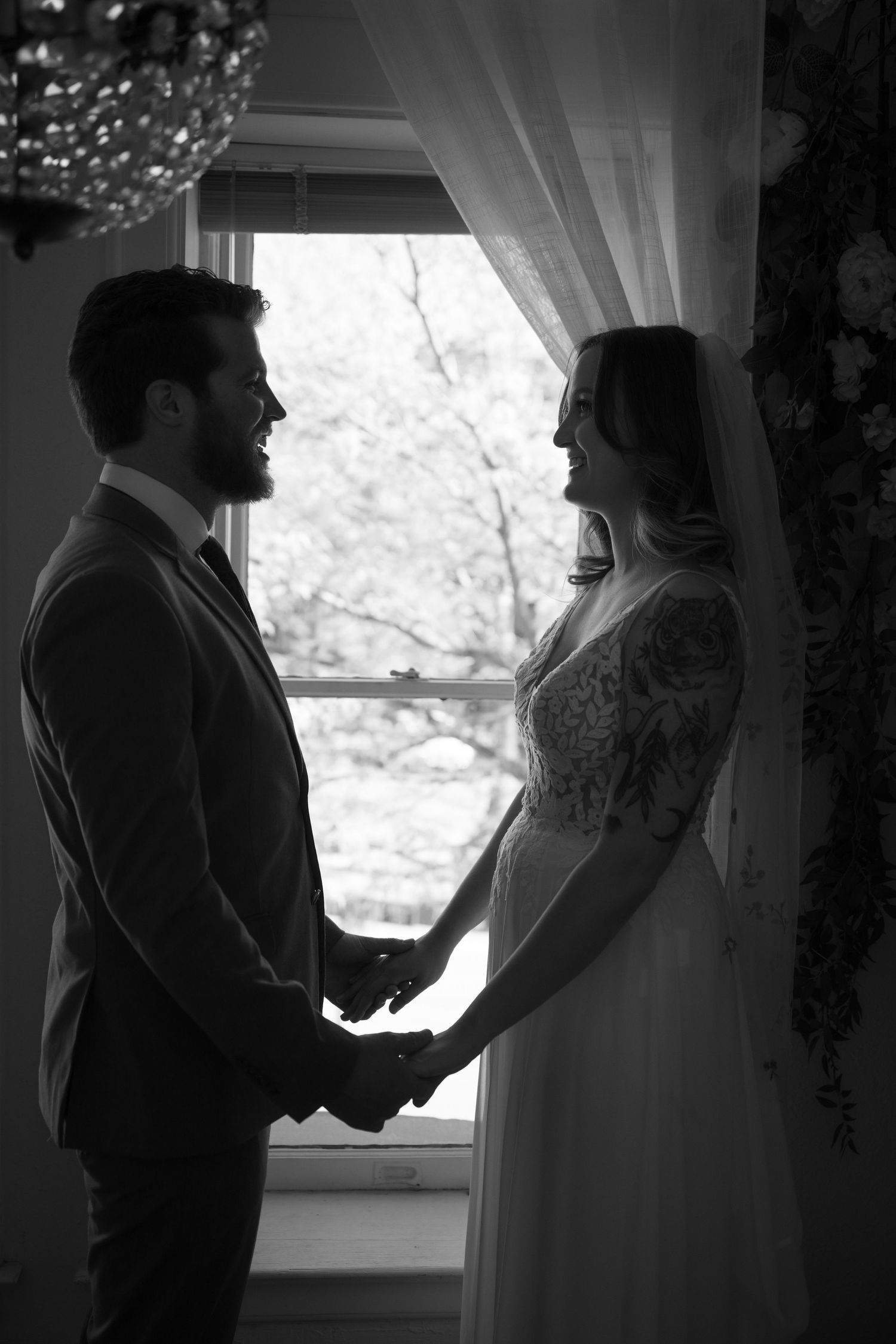 Silhouette of a couple holding hands by a window in intimate black and white wedding photography.