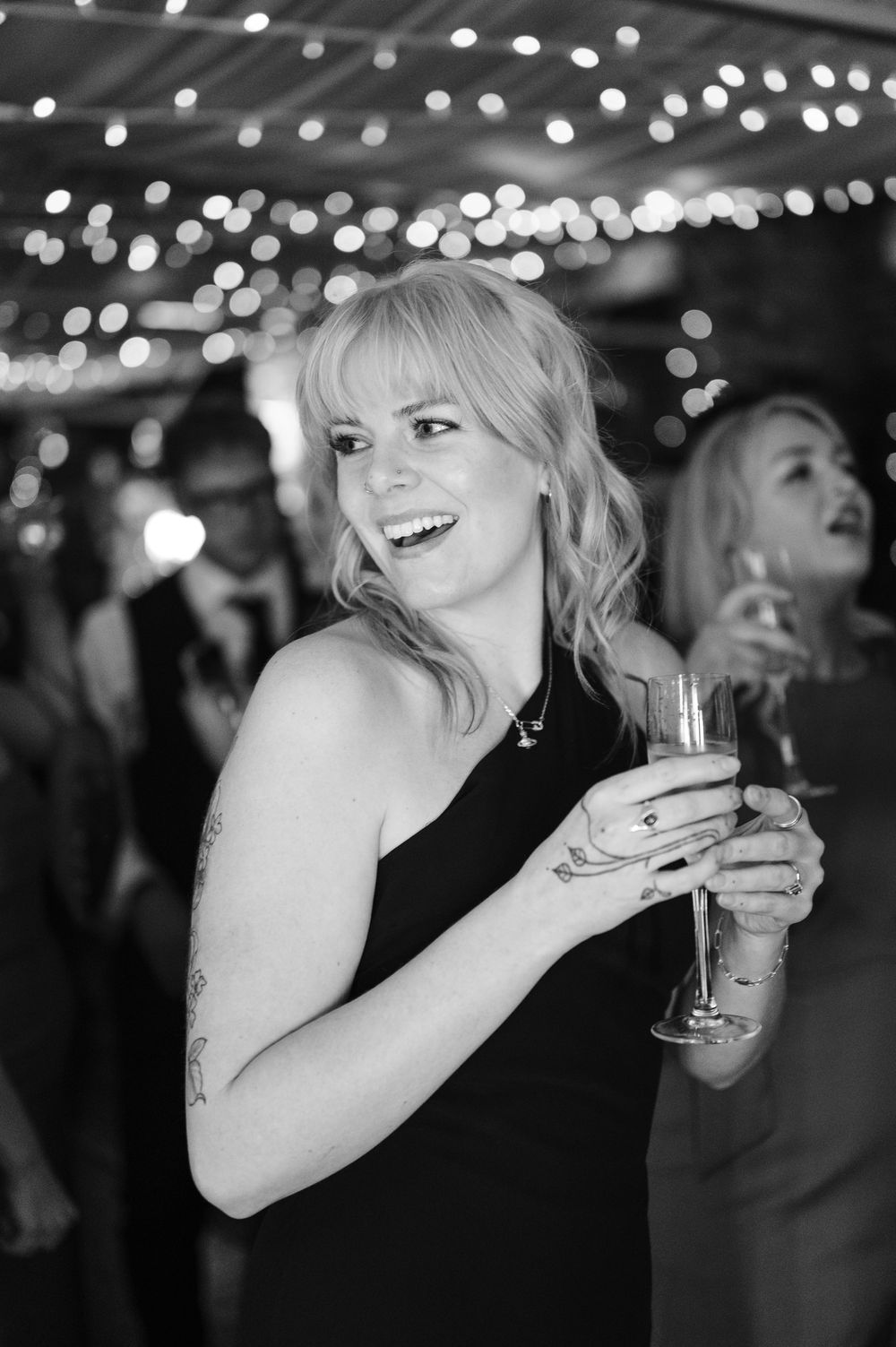 Black and white sequence of candid party moments showing someone laughing and holding a champagne glass under string lights.