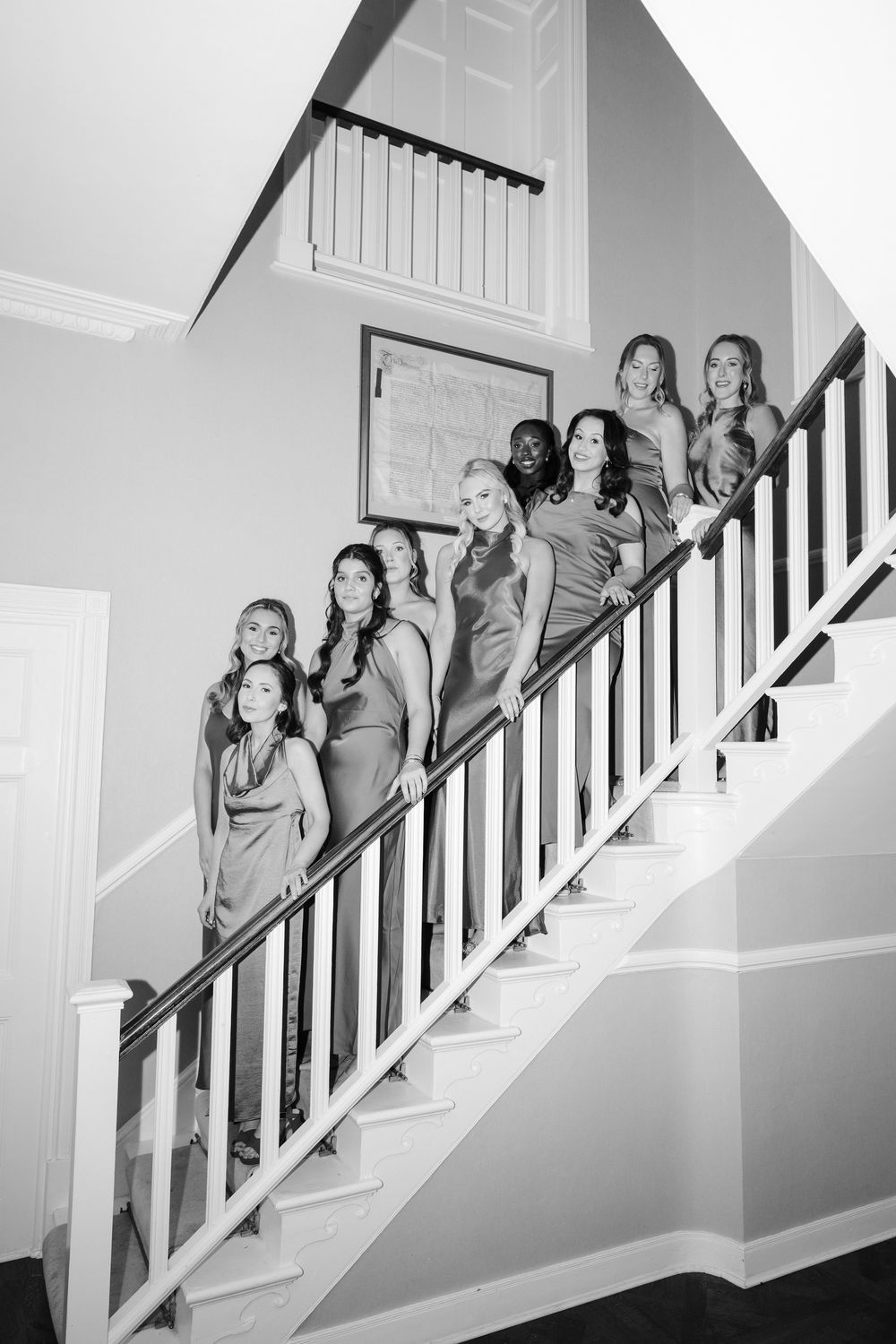 Black and white photo series showing a group posing playfully on a white staircase with dark railings.