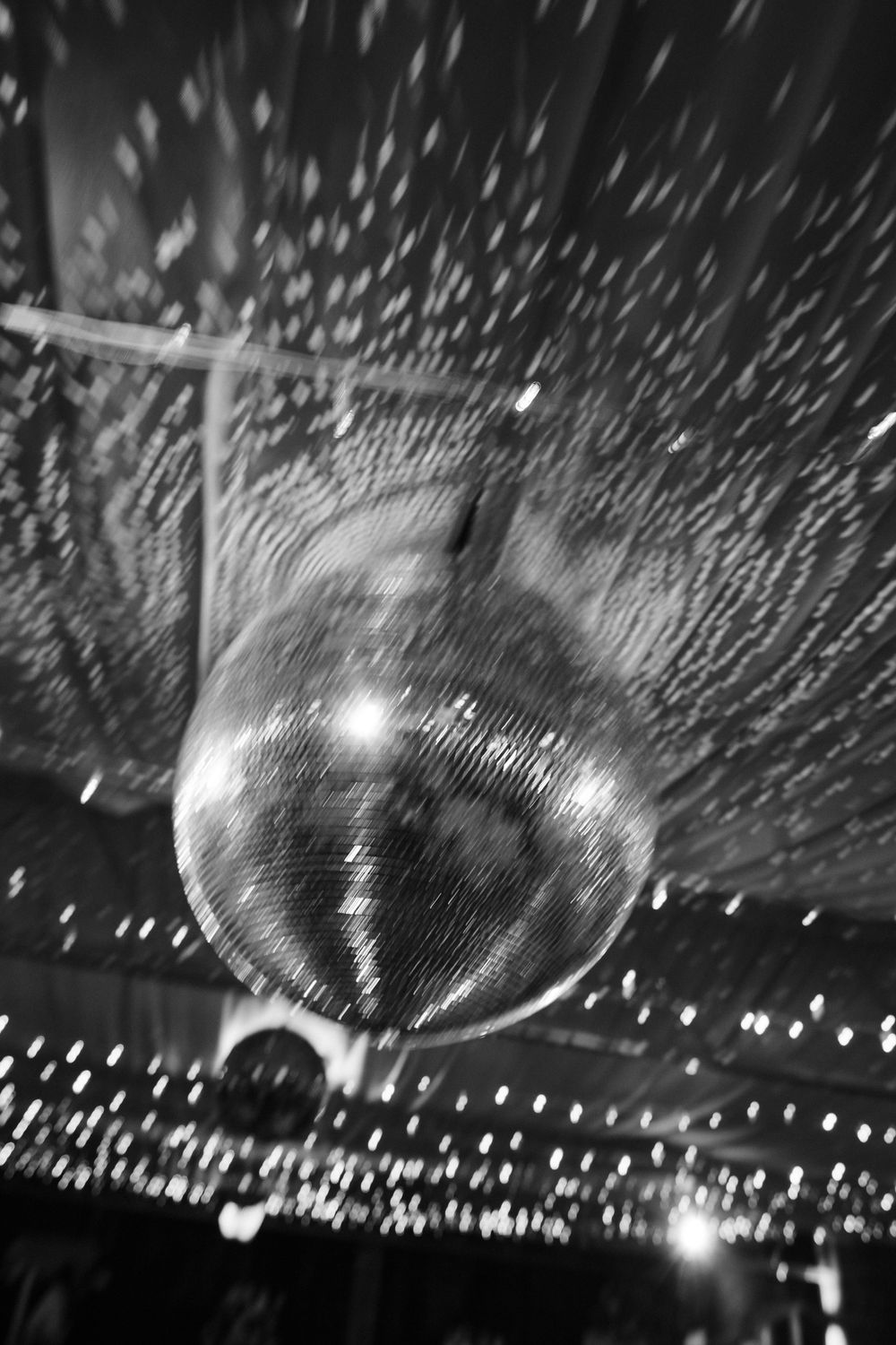 A large disco ball reflects shimmering light patterns across a dark venue ceiling during a party or event.