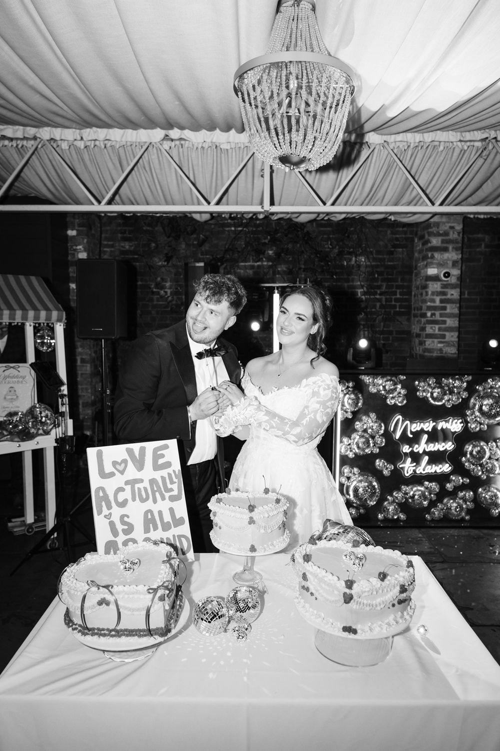 A black and white wedding reception photo showing a table decorated with cakes and floral arrangements.