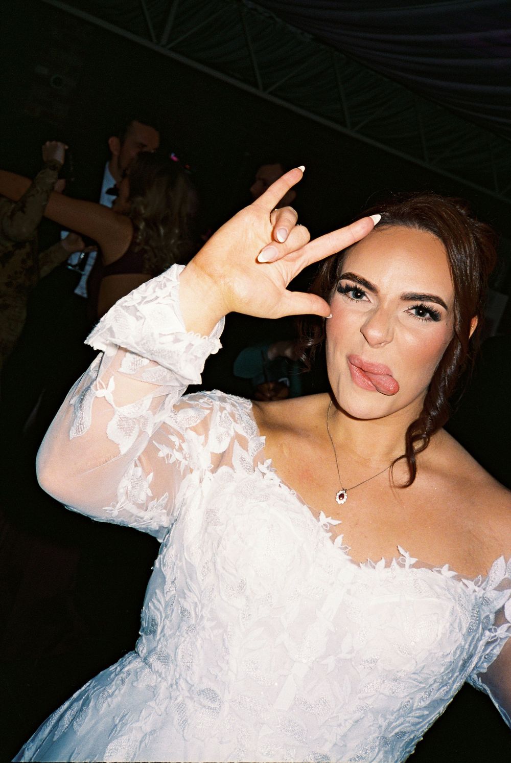 A bride in an off-shoulder white lace wedding gown poses during an evening celebration.