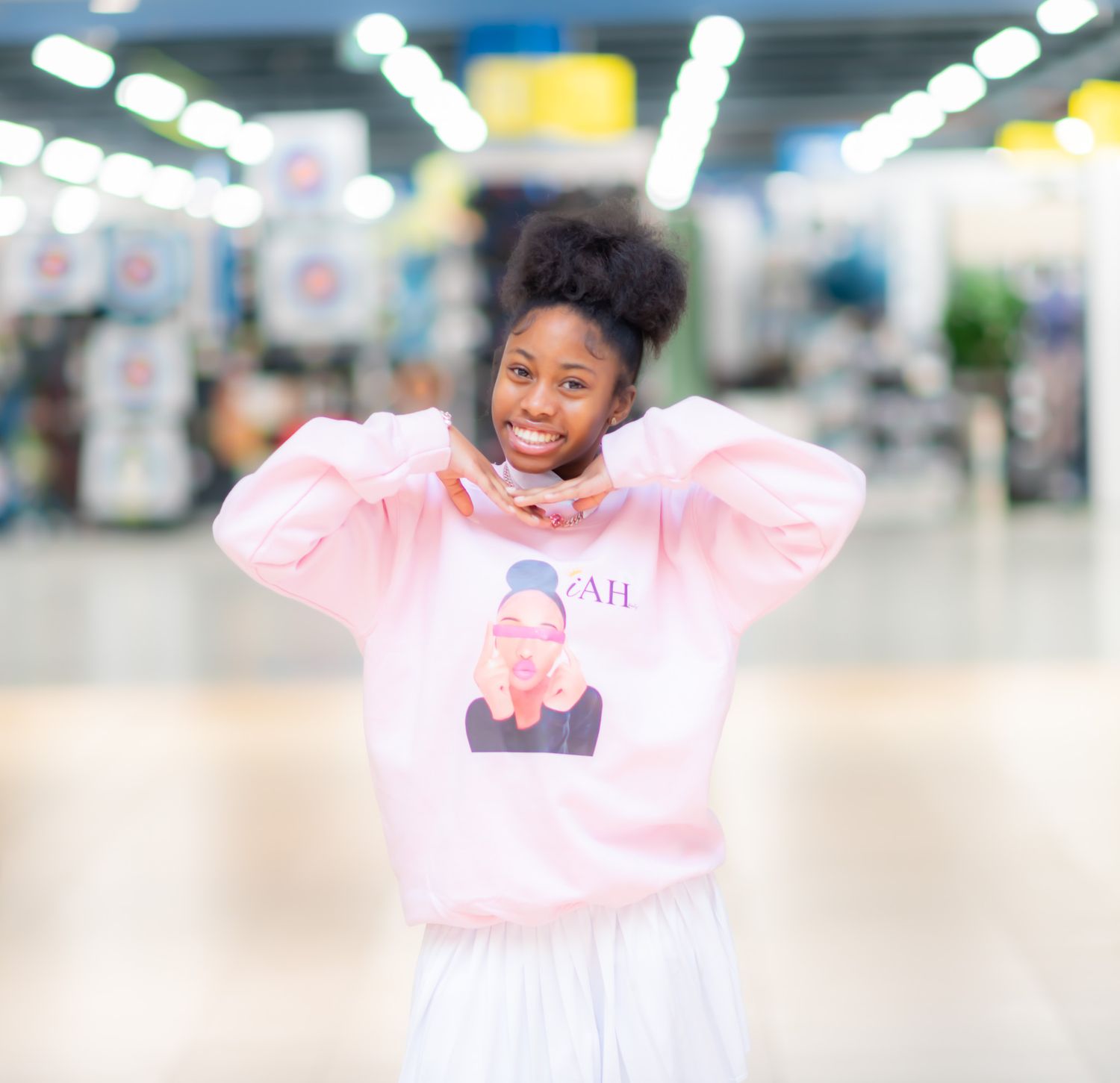 A child in a pink sweatshirt and tulle skirt poses playfully in a bright indoor setting.