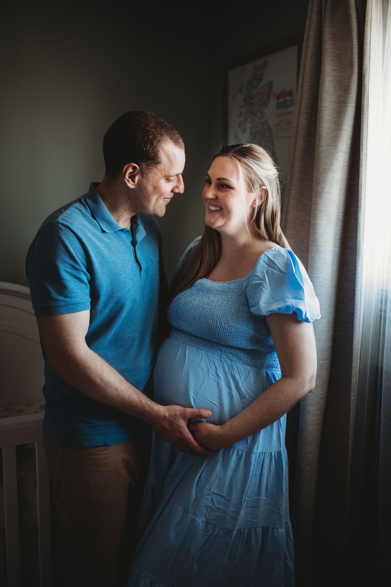 Expecting couple sharing an intimate moment together by a window in their home.