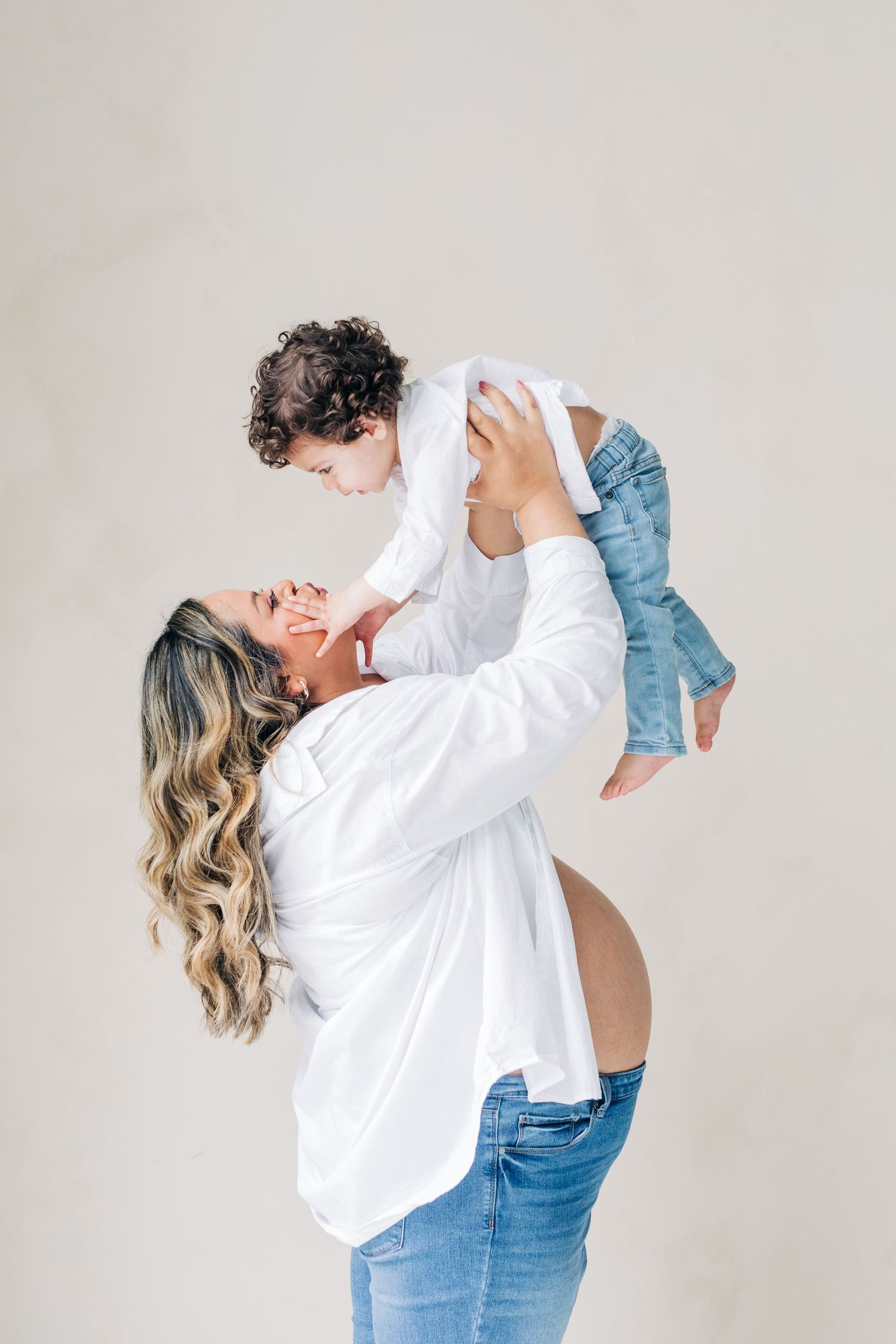 A parent wearing a white shirt and jeans lifts and plays with a small child in a series of joyful candid moments.