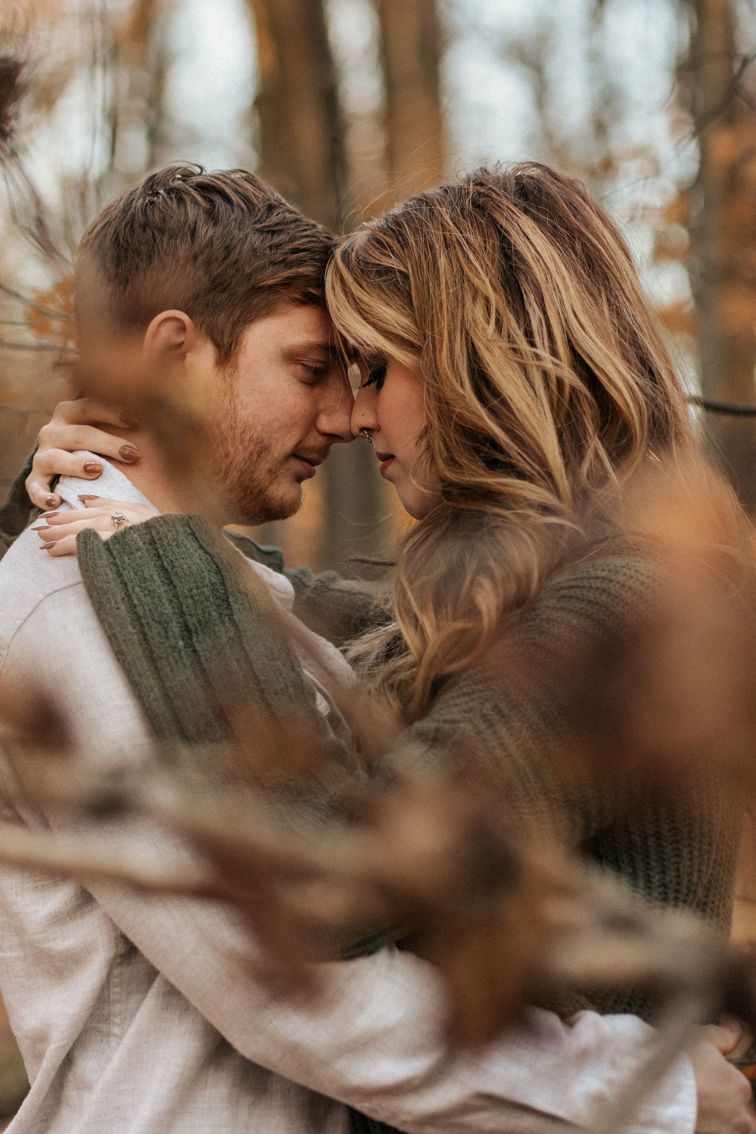 Romantic autumn couple in cozy sweaters embrace intimately in a forest setting with soft bokeh effect.