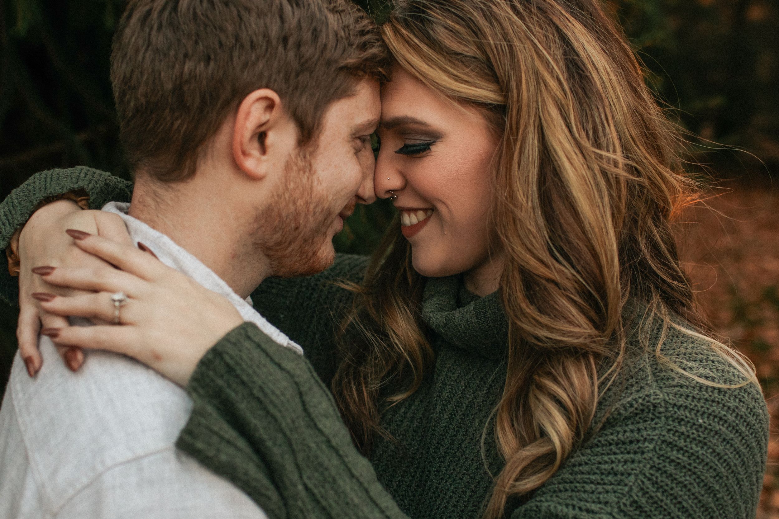 Couple embracing in cozy sweaters during outdoor fall photoshoot with warm tones.
