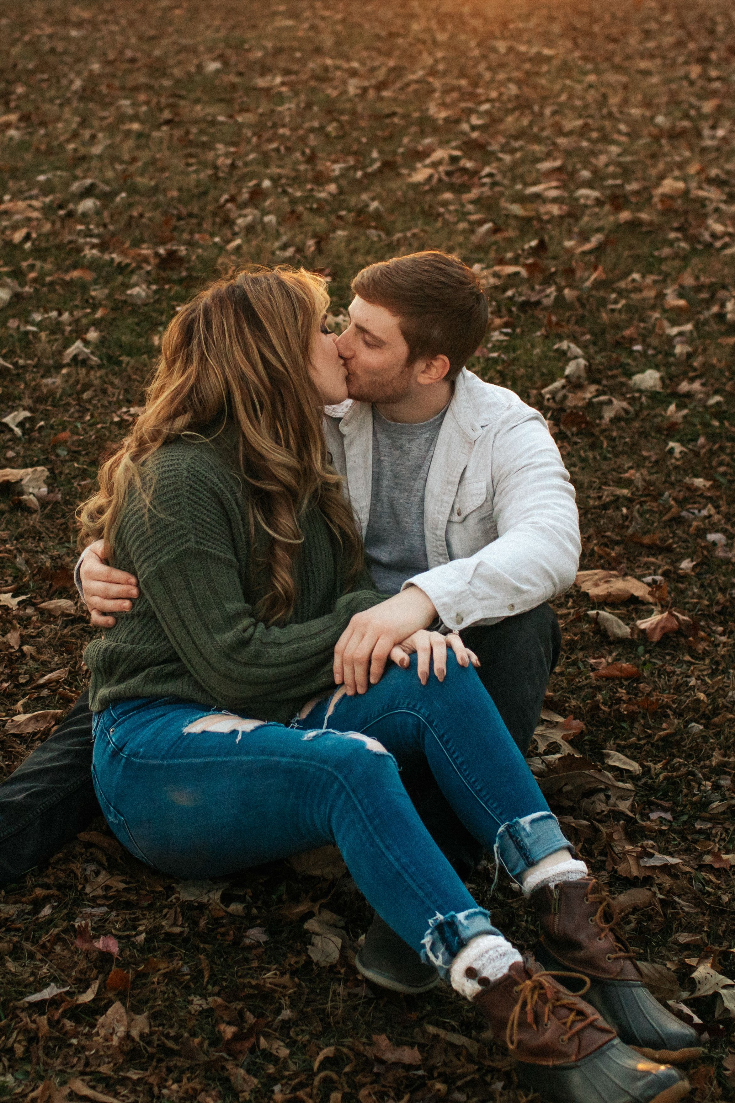 Couple sitting together on fallen autumn leaves in a romantic outdoor setting.