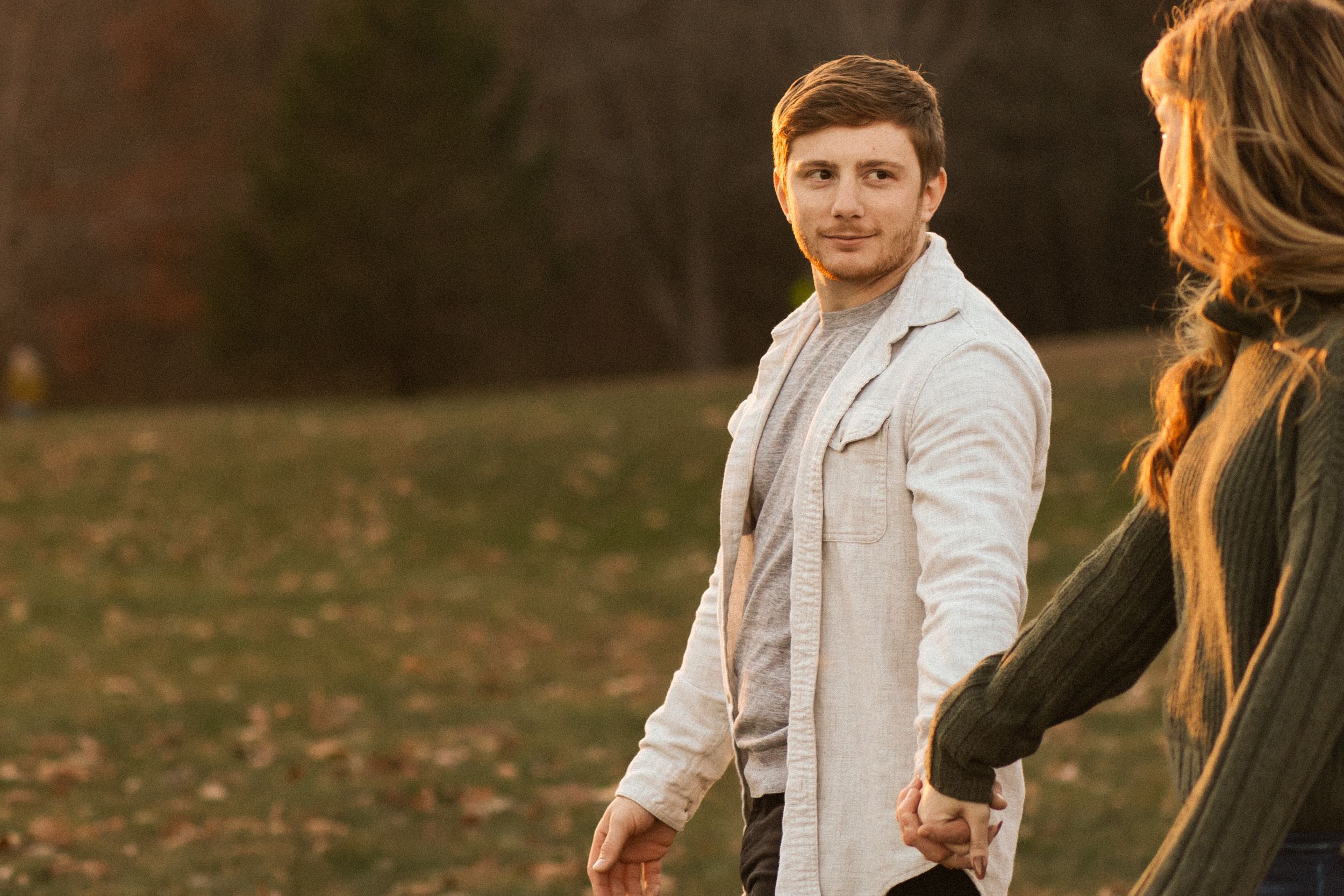 A couple shares a romantic moment in a golden autumn forest setting during sunset.