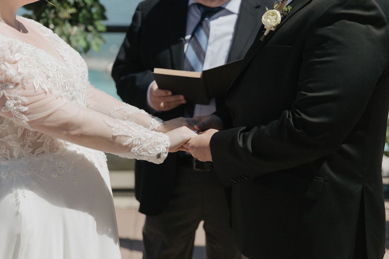 Couple exchanges vows holding hands while officiant reads from a book during an intimate wedding ceremony.