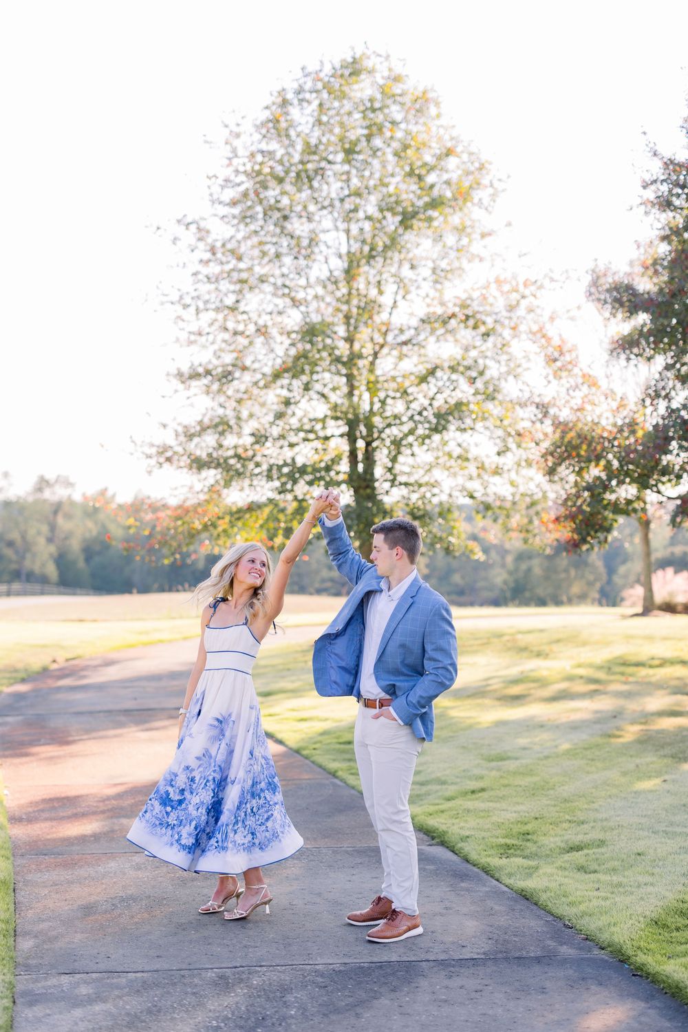 A couple shares a romantic moment in a park at sunset, with the woman in a blue and white dress and man in light attire.