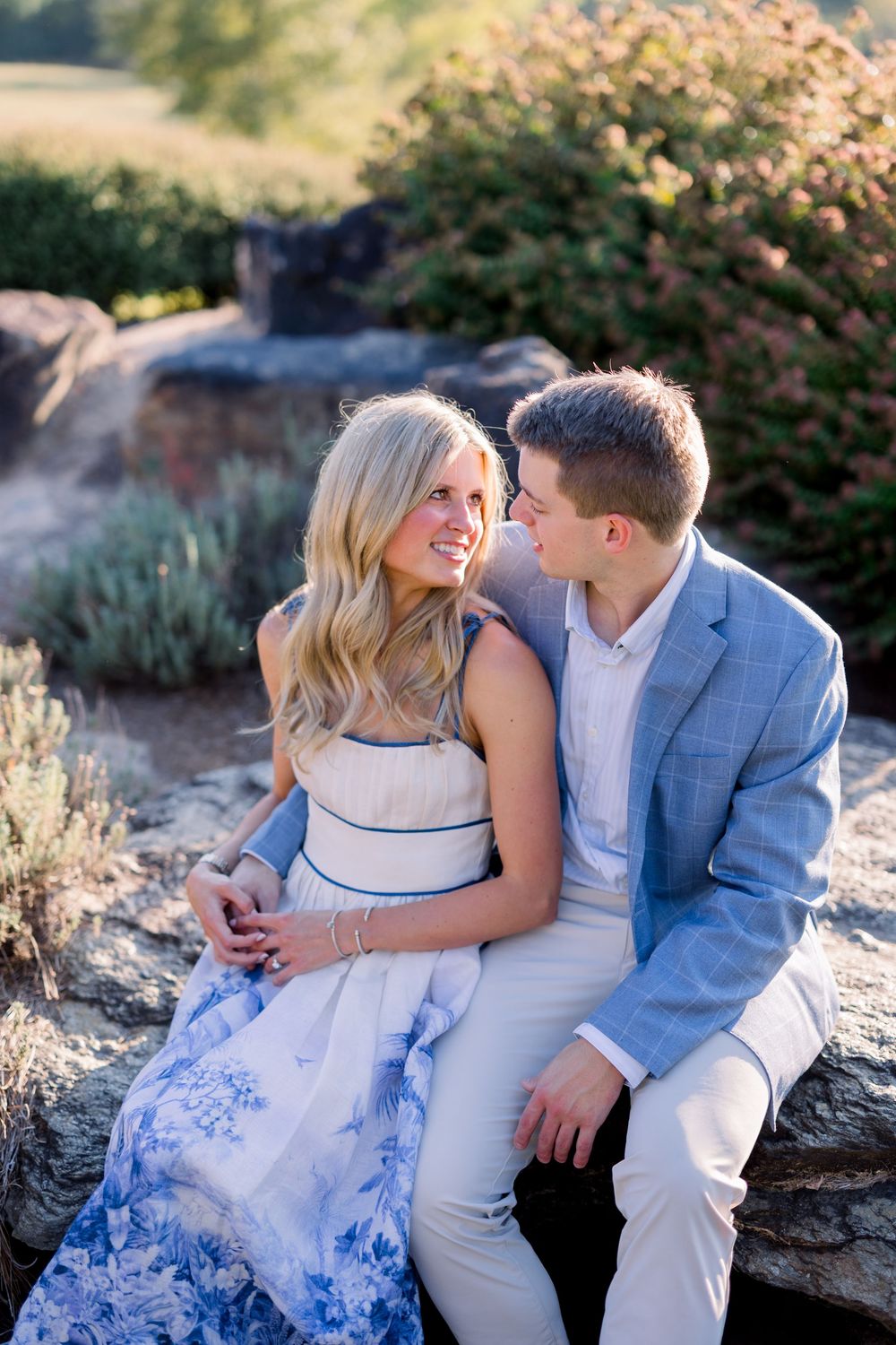 Romantic couple in coordinated blue and white outfits pose together on rocky outcrop during outdoor photoshoot.