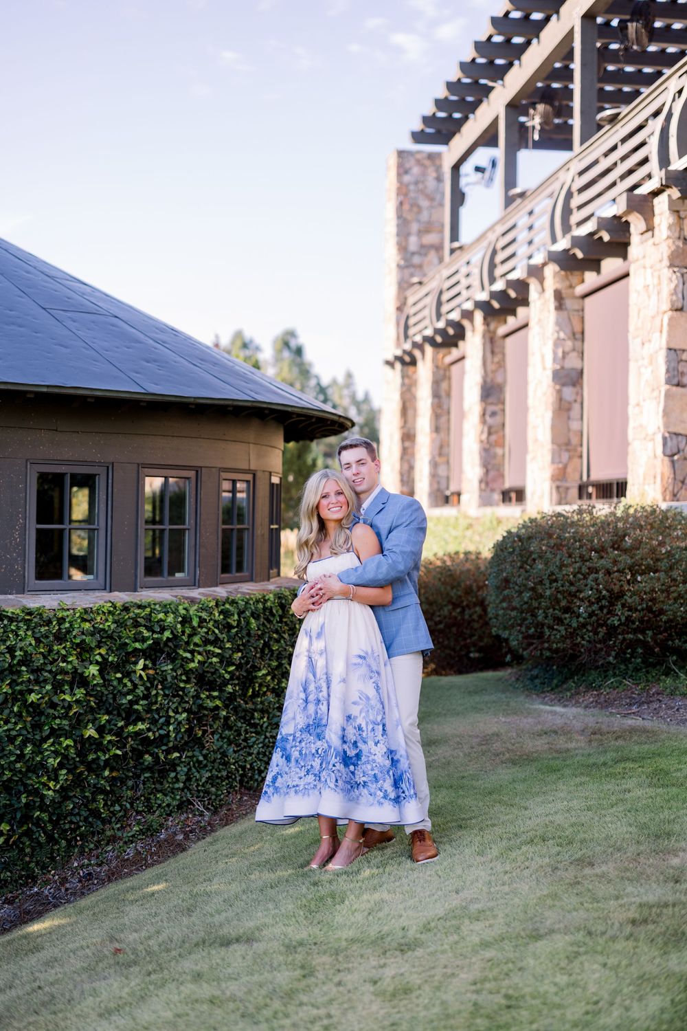 Couple in matching blue and white attire pose together on grassy lawn near modern building exterior.
