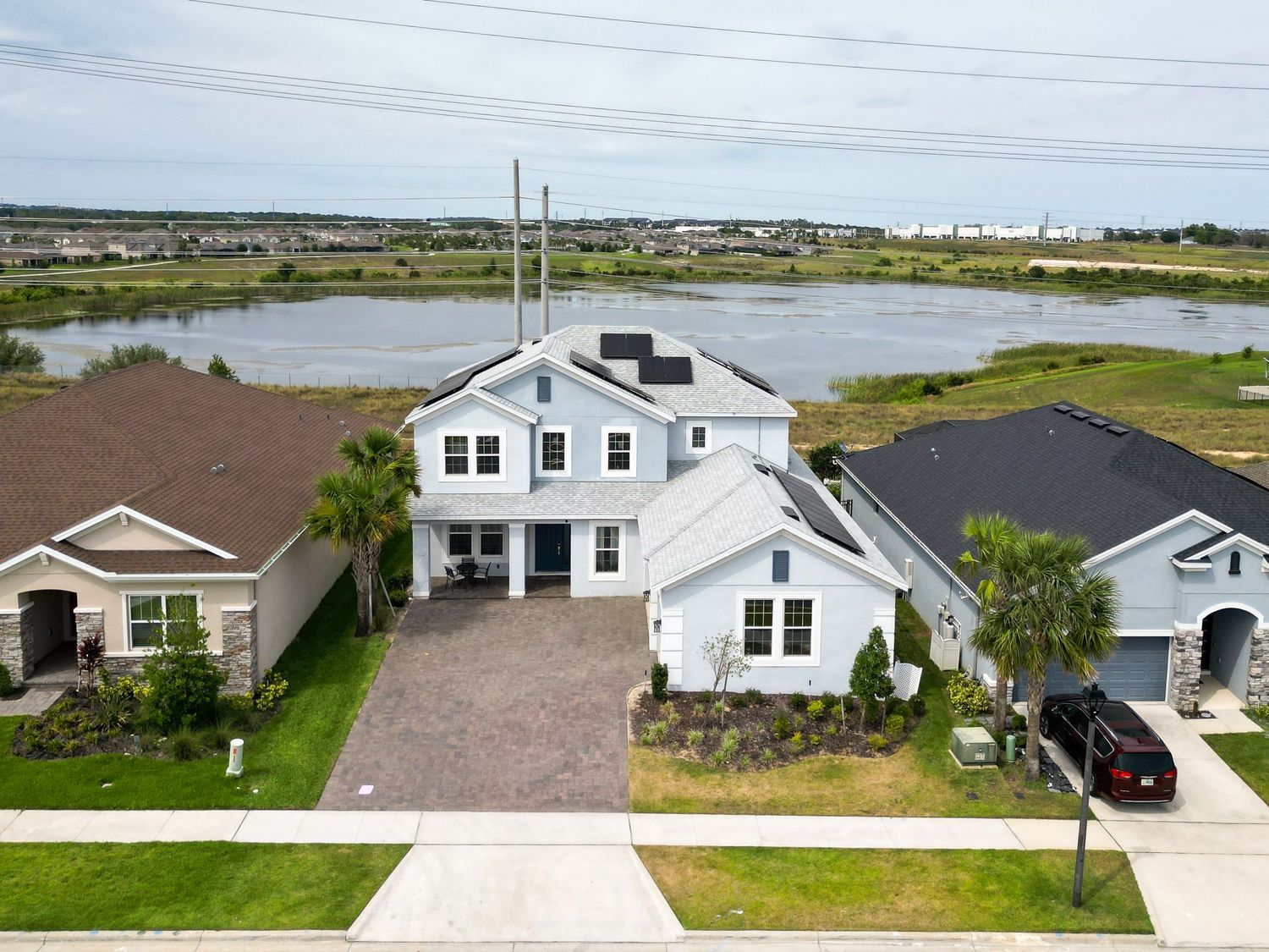 Modern two-story coastal home with dark gray garage doors and vibrant landscaping against a dramatic purple sunset sky.