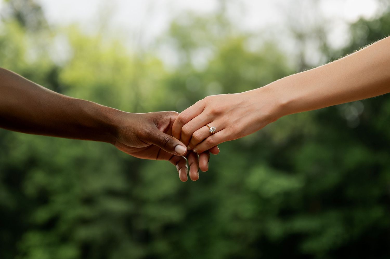 Two hands reach out to touch each other against a blurred natural background.