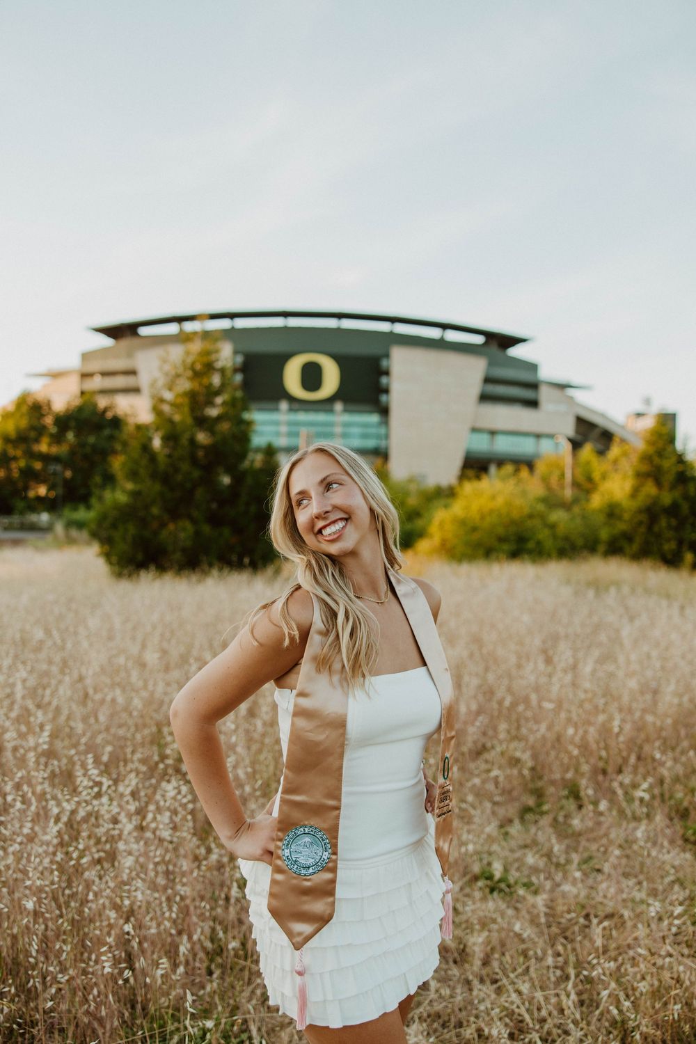 Outdoor portrait session in tall grass field with modern building in background.