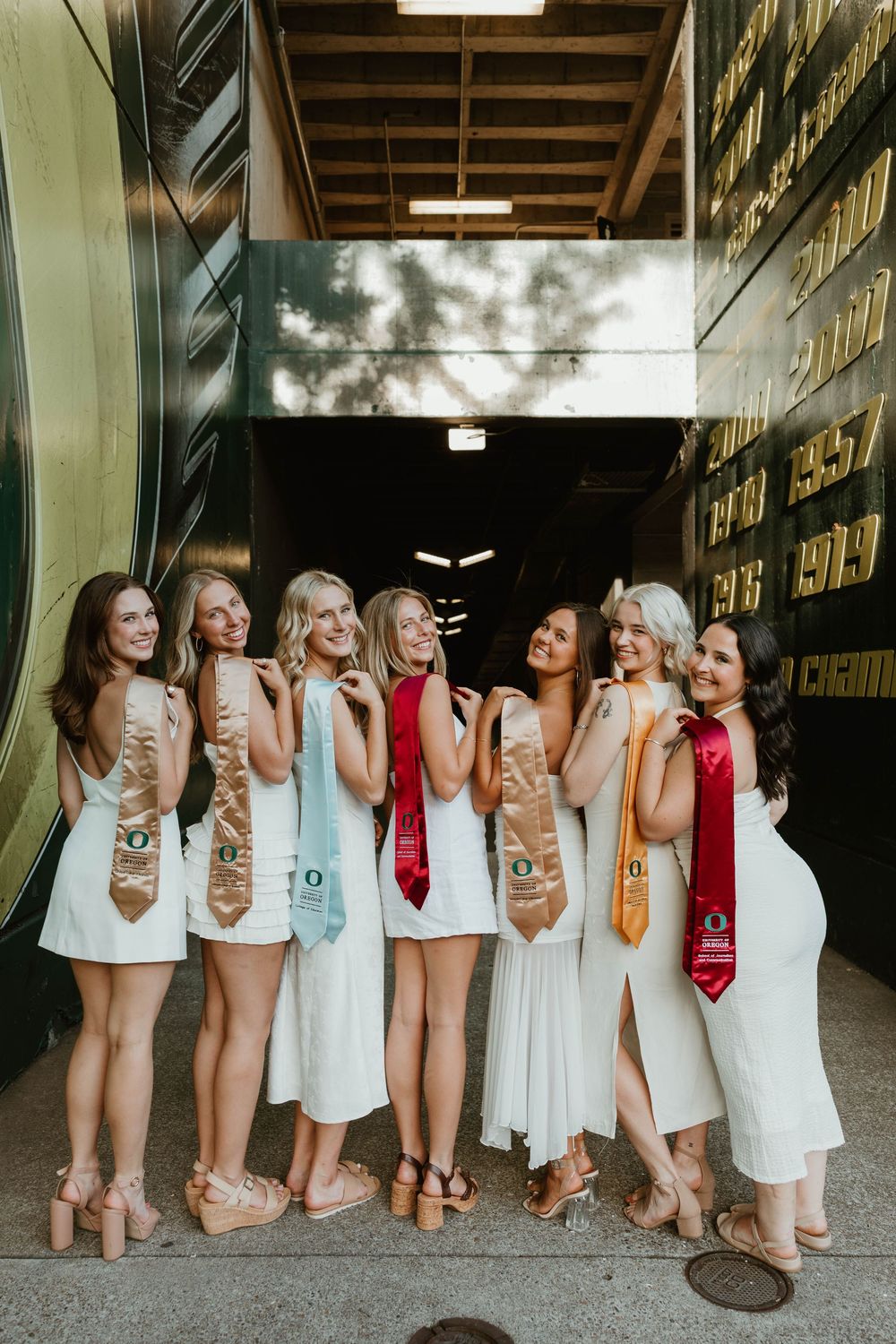 A group poses together in white dresses and red accessories while sitting along a rustic barn wall.