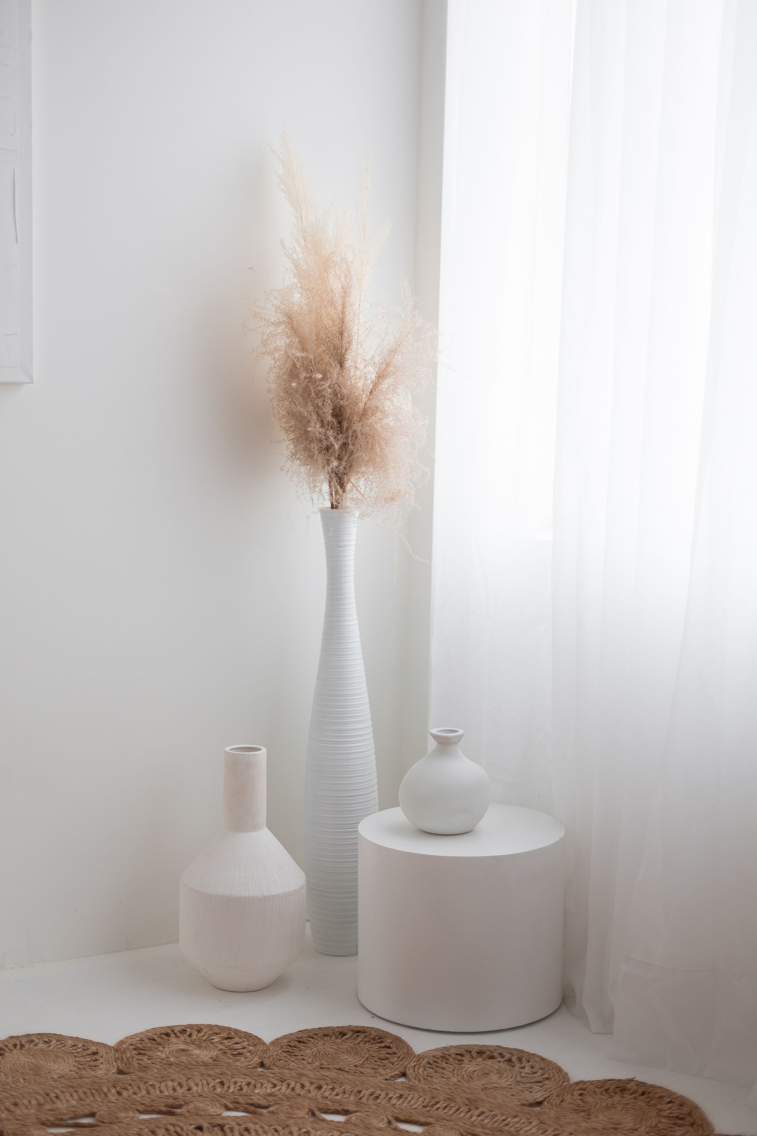 White minimalist corner with tall vase holding pampas grass and two small ceramic vases.