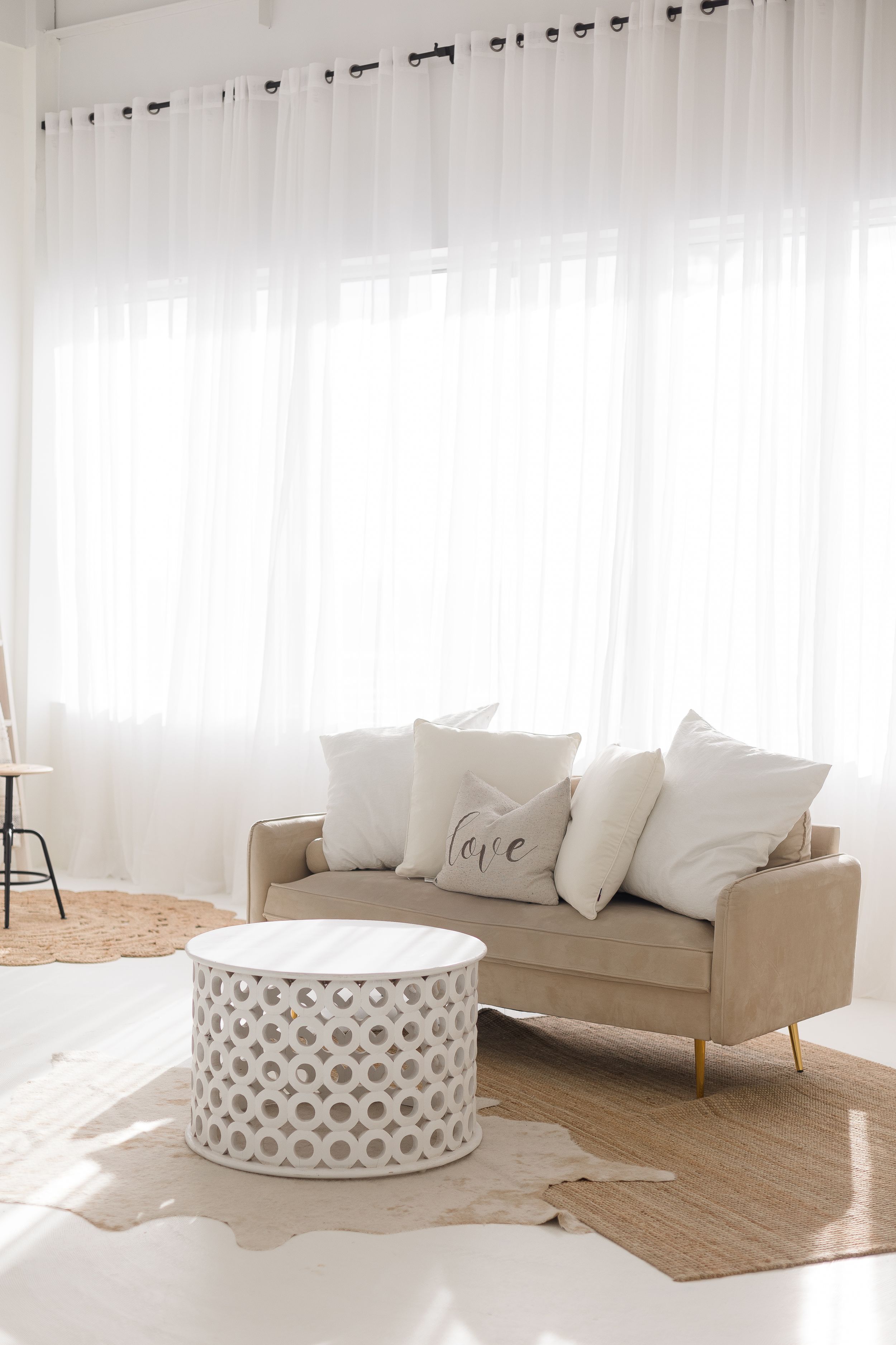 Bright minimalist living room with beige sofa, white curtains, and a round decorative coffee table.