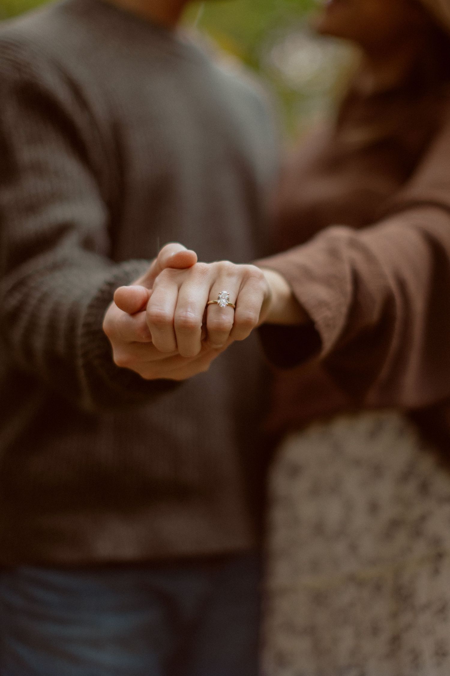 A close-up of a couple's intertwined hands showing a woman's diamond engagement ring at a Kansas City engagement photo session.