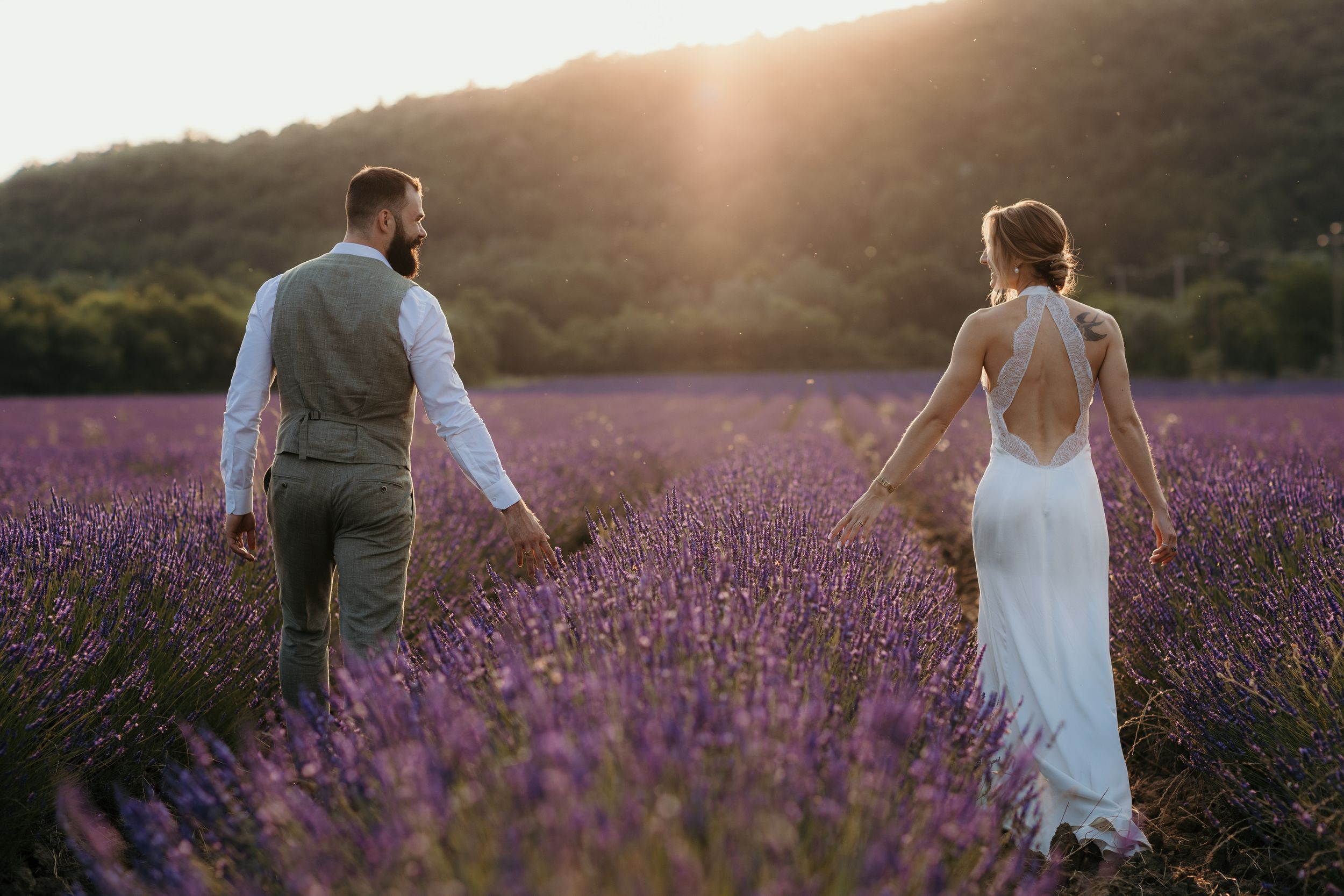 A couple walks through a vibrant purple lavender field at sunset creating a romantic silhouette against the sky.