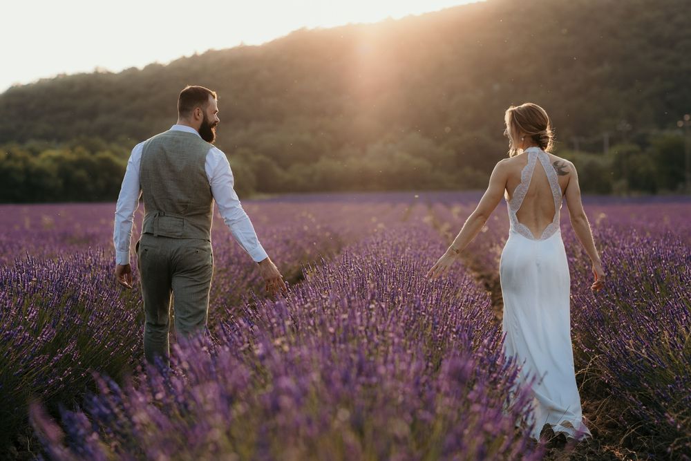 A couple walks through a vibrant purple lavender field at sunset creating a romantic silhouette against the sky.
