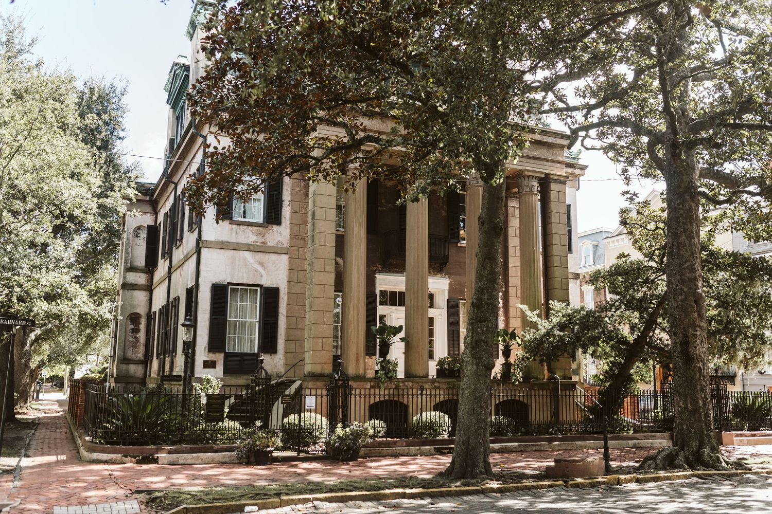 Historic southern mansion with white columns stands elegantly among mature oak trees on a sunny day.
