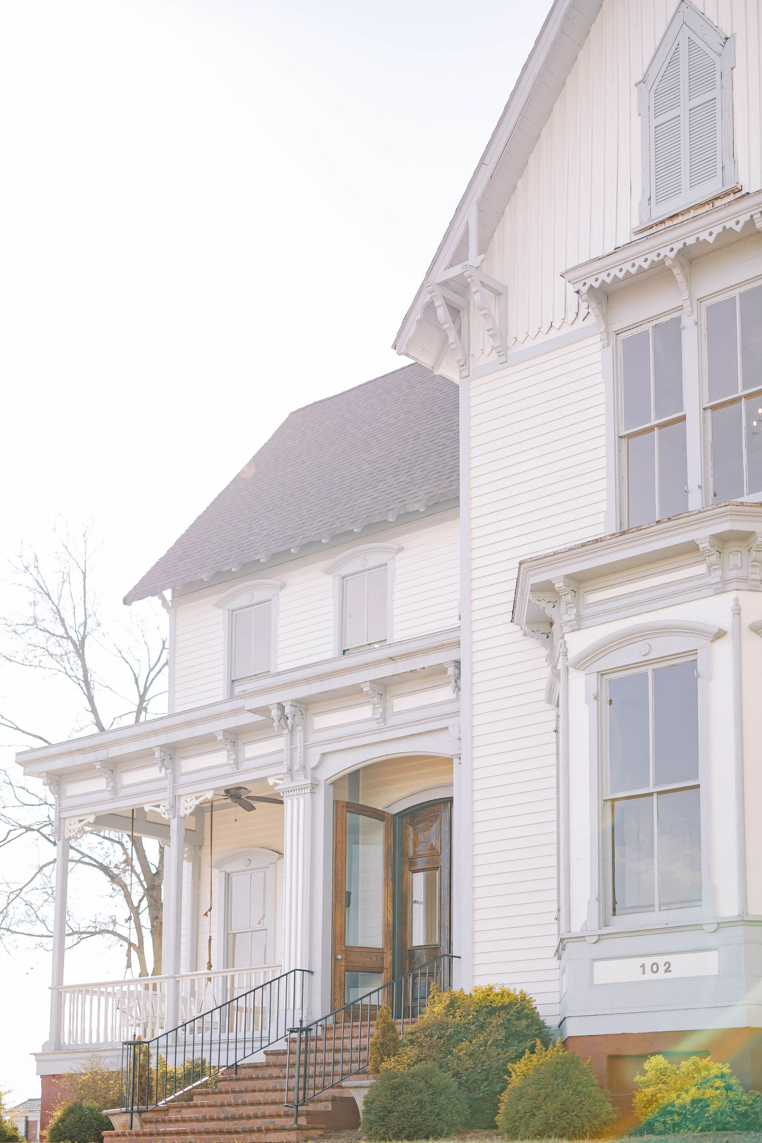 White Victorian-style houses with ornate trim and landscaping line a residential street in a historic neighborhood.
