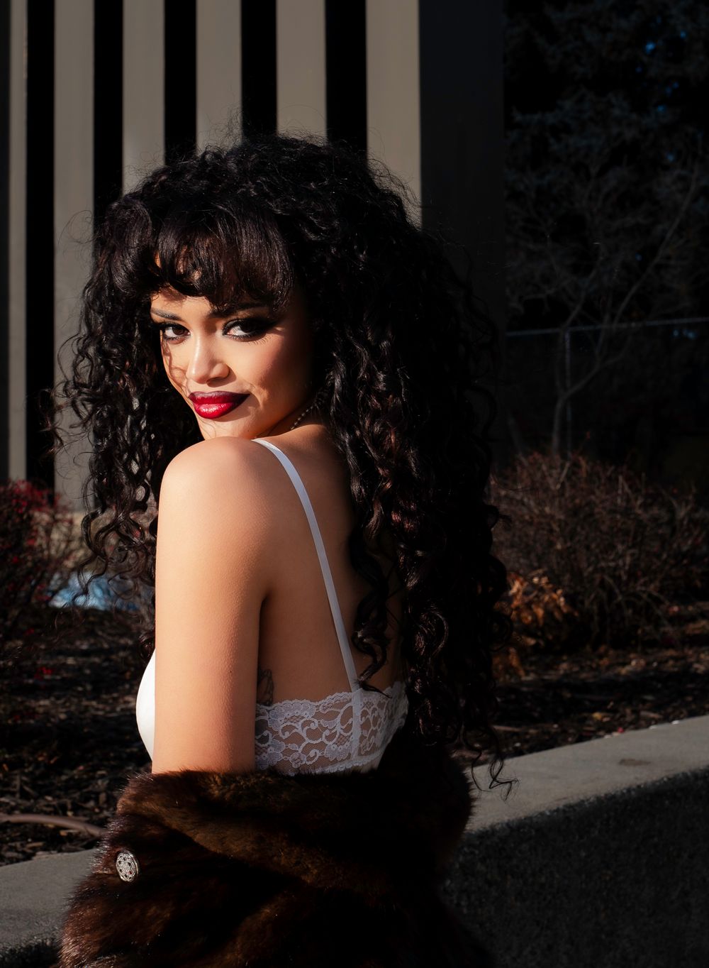 Glamour portrait with curly hair and fur wrap against striped background.