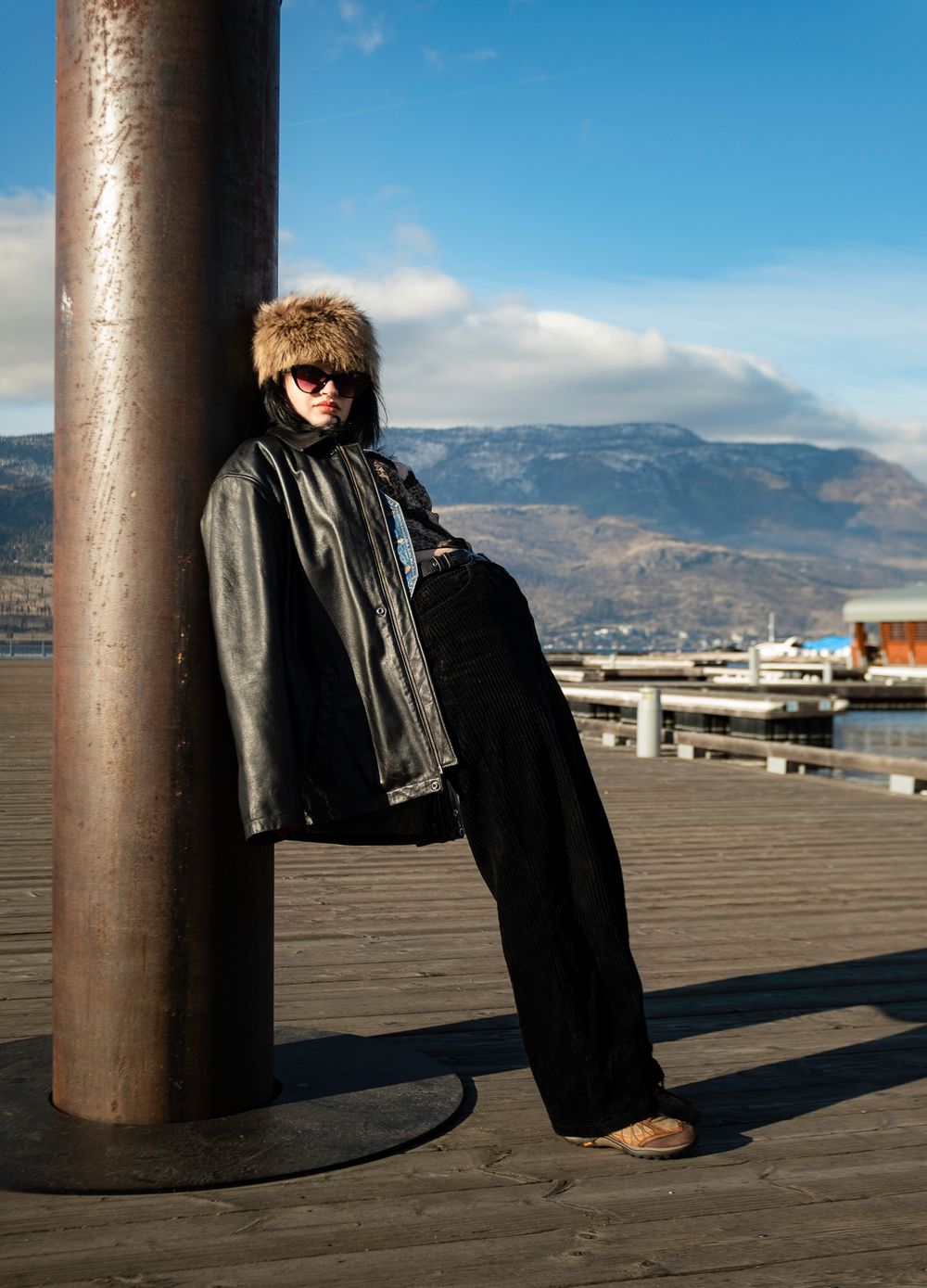 Fashion shot on pier with model in winter wear against mountain backdrop.