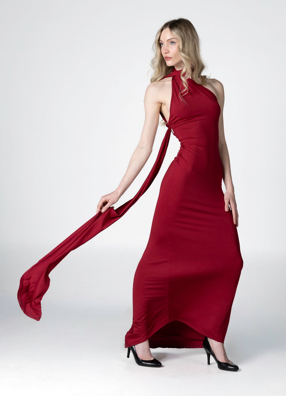 Elegant red floor-length dress with flowing sash detail and halter neckline shown in fashion photography against white backdrop.