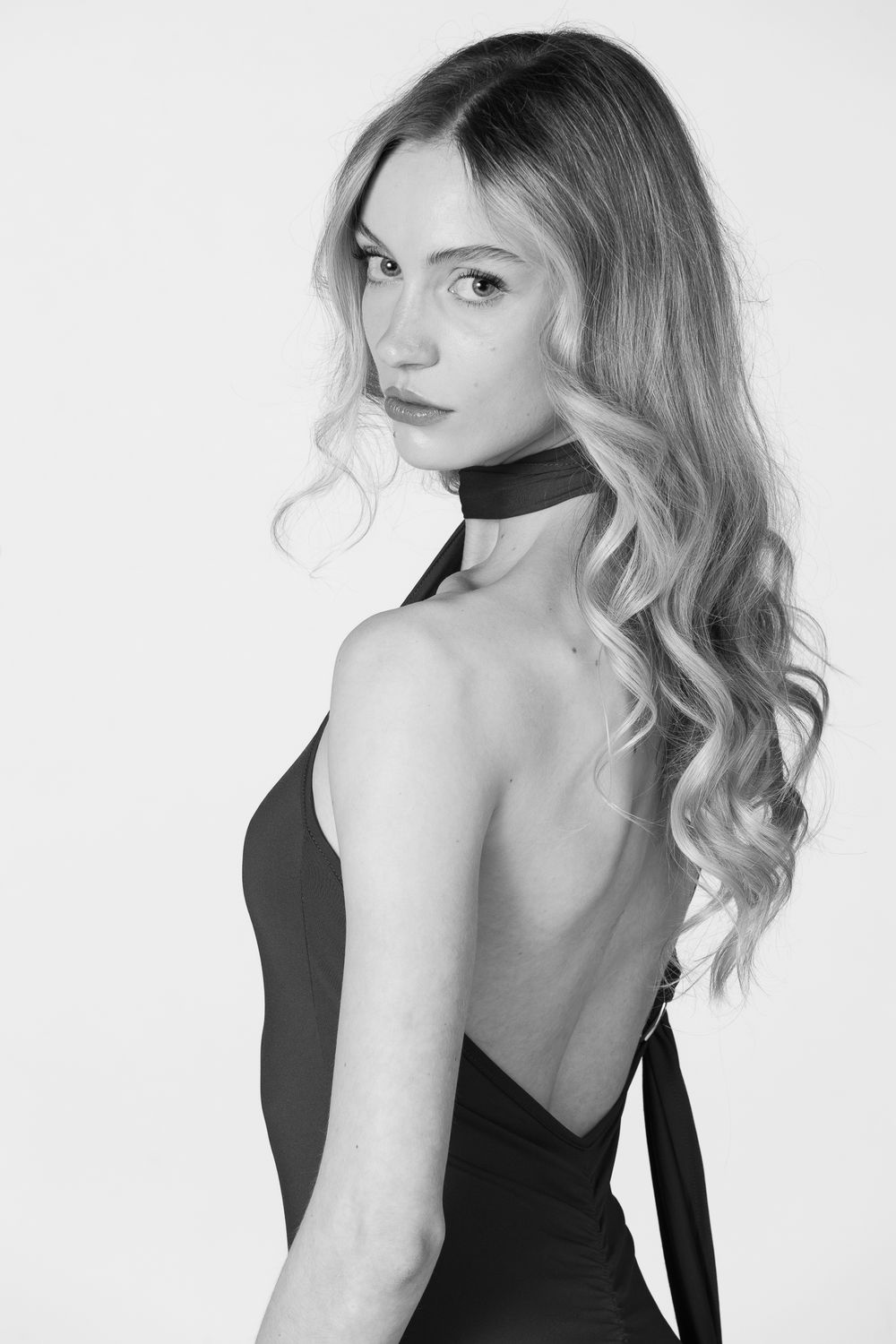 Black and white portrait of model in backless halter dress with wavy blonde hair.