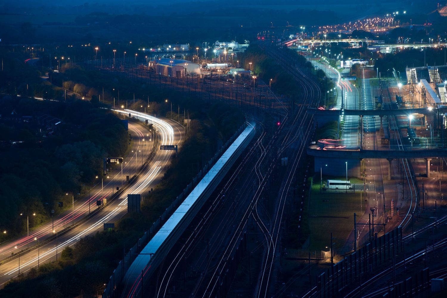 Aerial nighttime view of illuminated railway tracks and roads in an urban setting.