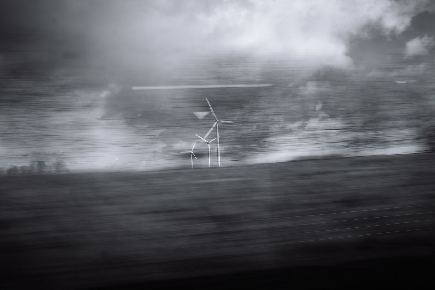 Moody black and white landscape with wind turbines emerging through fog.