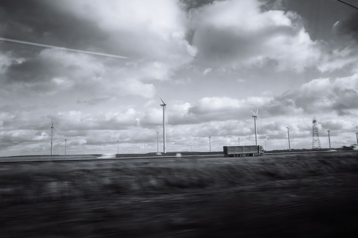 Wind turbines and power lines silhouetted against dramatic cloudy sky.
