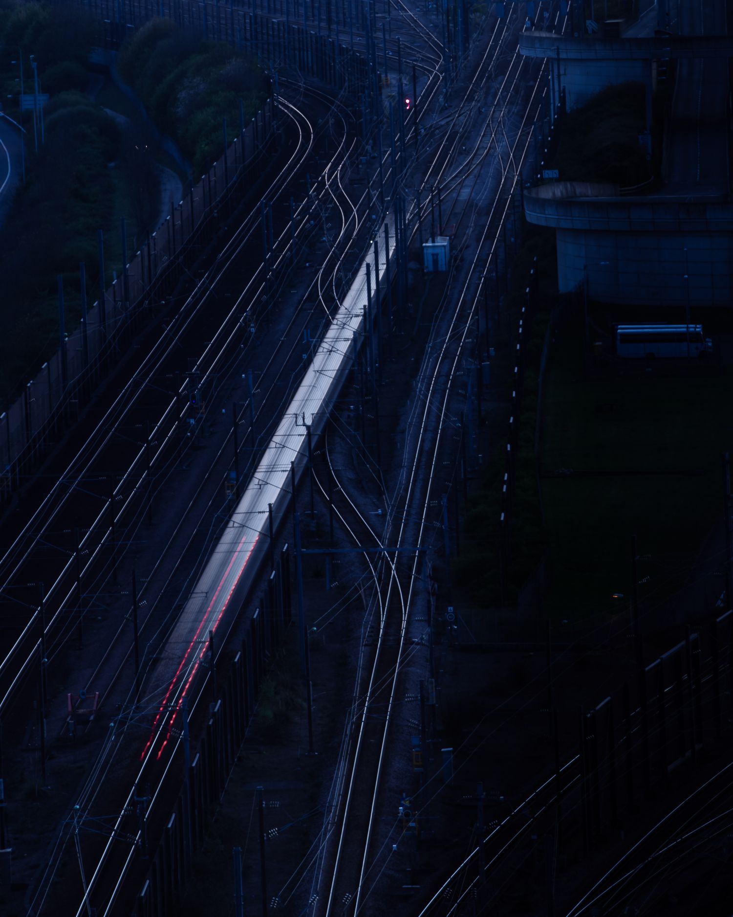 Aerial view of illuminated railway tracks converging through dark urban landscape.