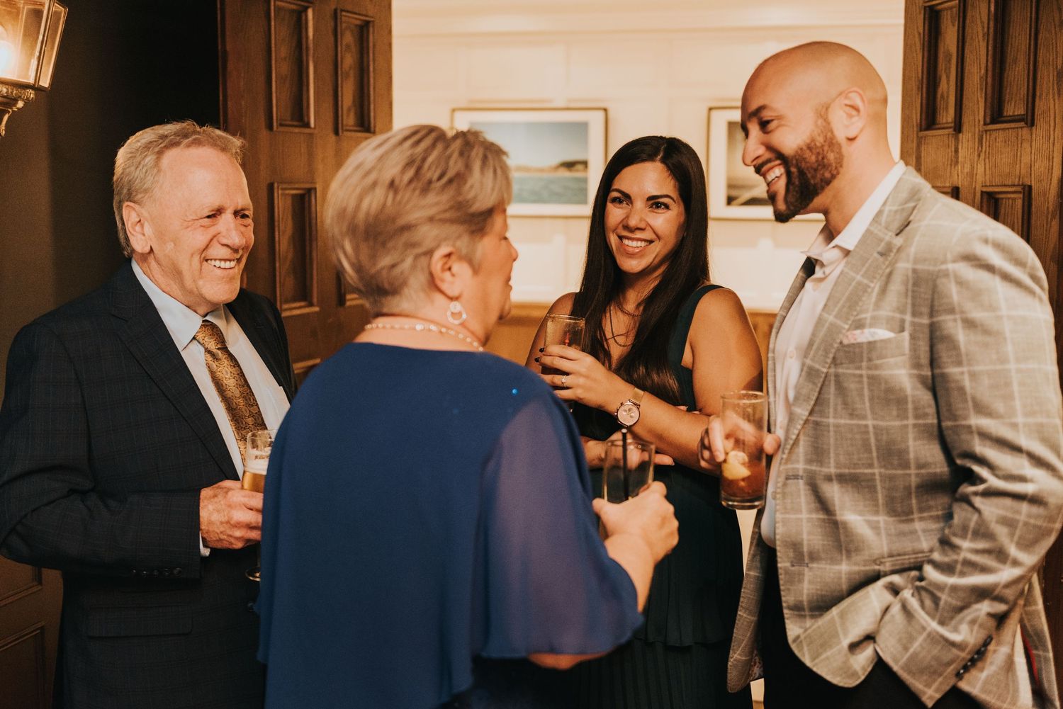 A group of people engaged in conversation at an indoor event wearing formal attire.