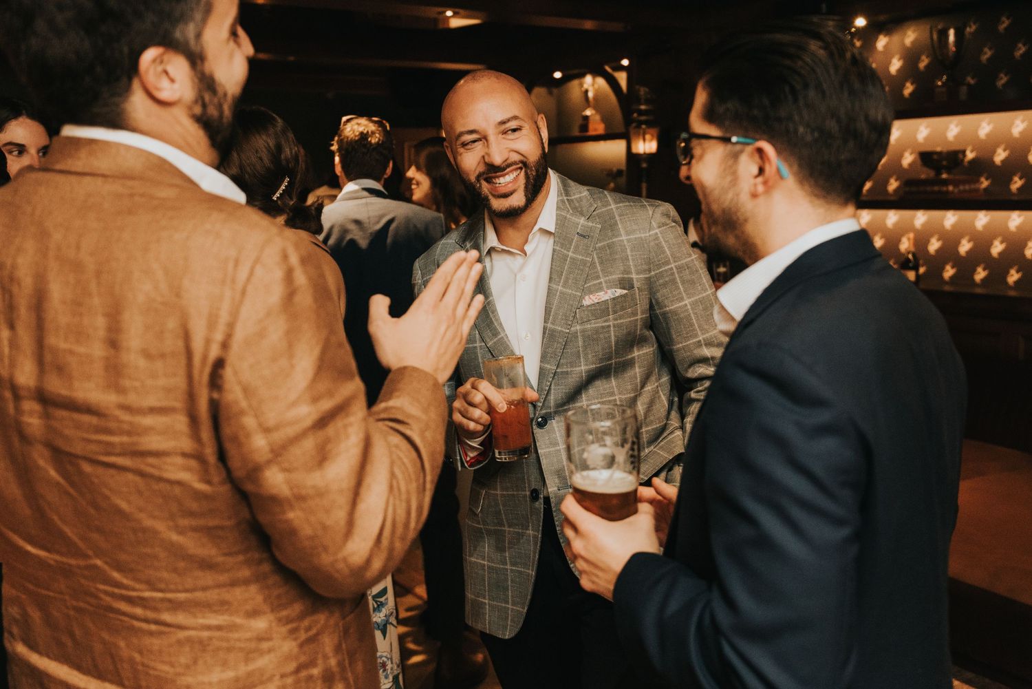 A group of people enjoying drinks and conversation at a dimly lit upscale bar or lounge.