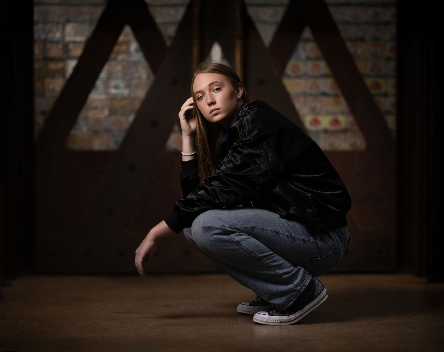 A young woman in dark clothing poses against a rustic brick wall background.