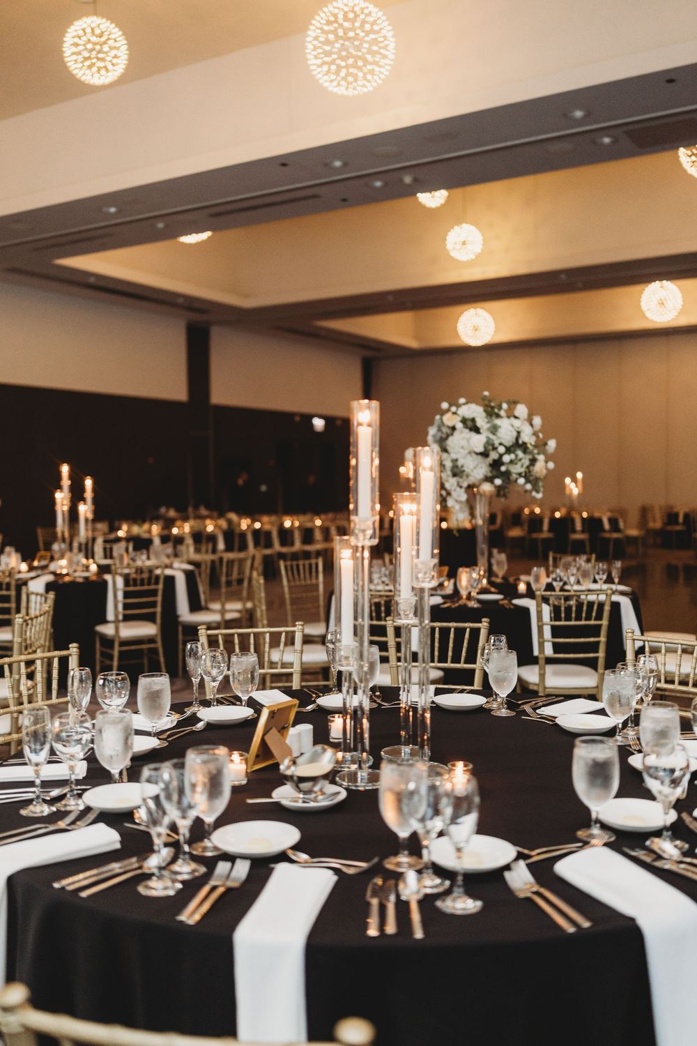 Elegant wedding reception venue with black tablecloths, tall candlesticks, and white floral centerpieces in a modern ballroom.