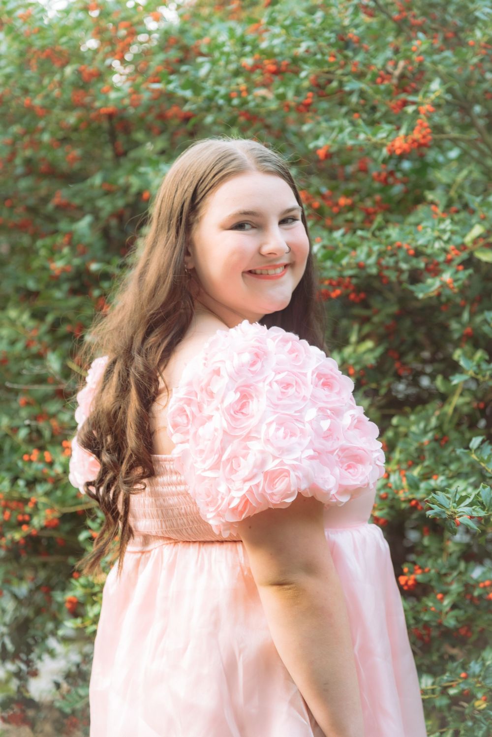 Graduate holding pink roses against flowering bush background.