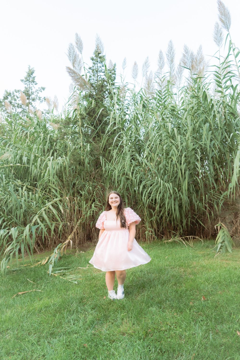 A pink dress flows in the breeze against tall green reeds in a garden setting.