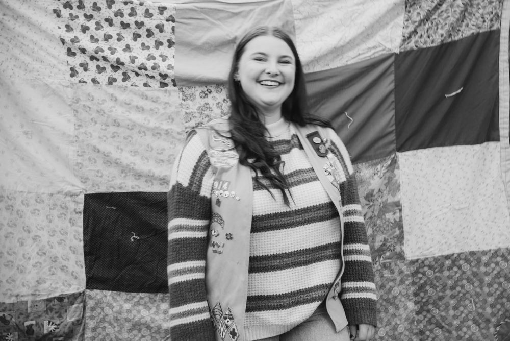 Someone wearing a striped sweater poses in front of a patterned backdrop.
