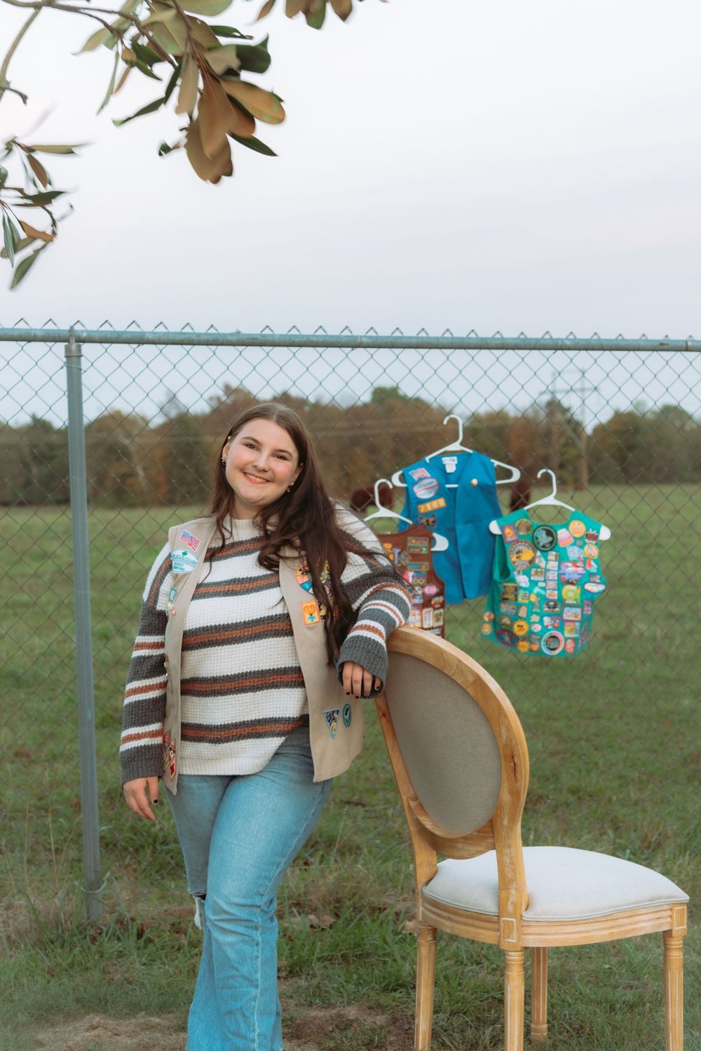 A vintage wooden chair sits against a chain link fence with blue clothing displayed.
