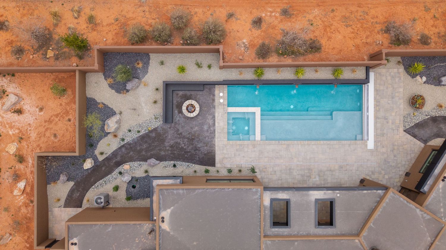 Aerial drone view of a modern rectangular swimming pool surrounded by desert landscape and concrete decking.