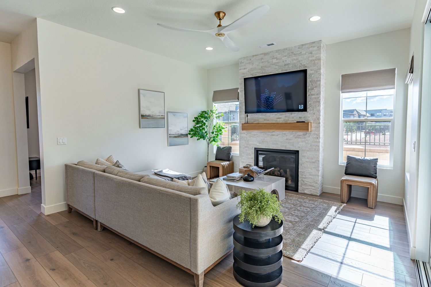 Modern living room with gray sofa, wood-burning fireplace, hardwood floors, ceiling fan, and wall-mounted TV.