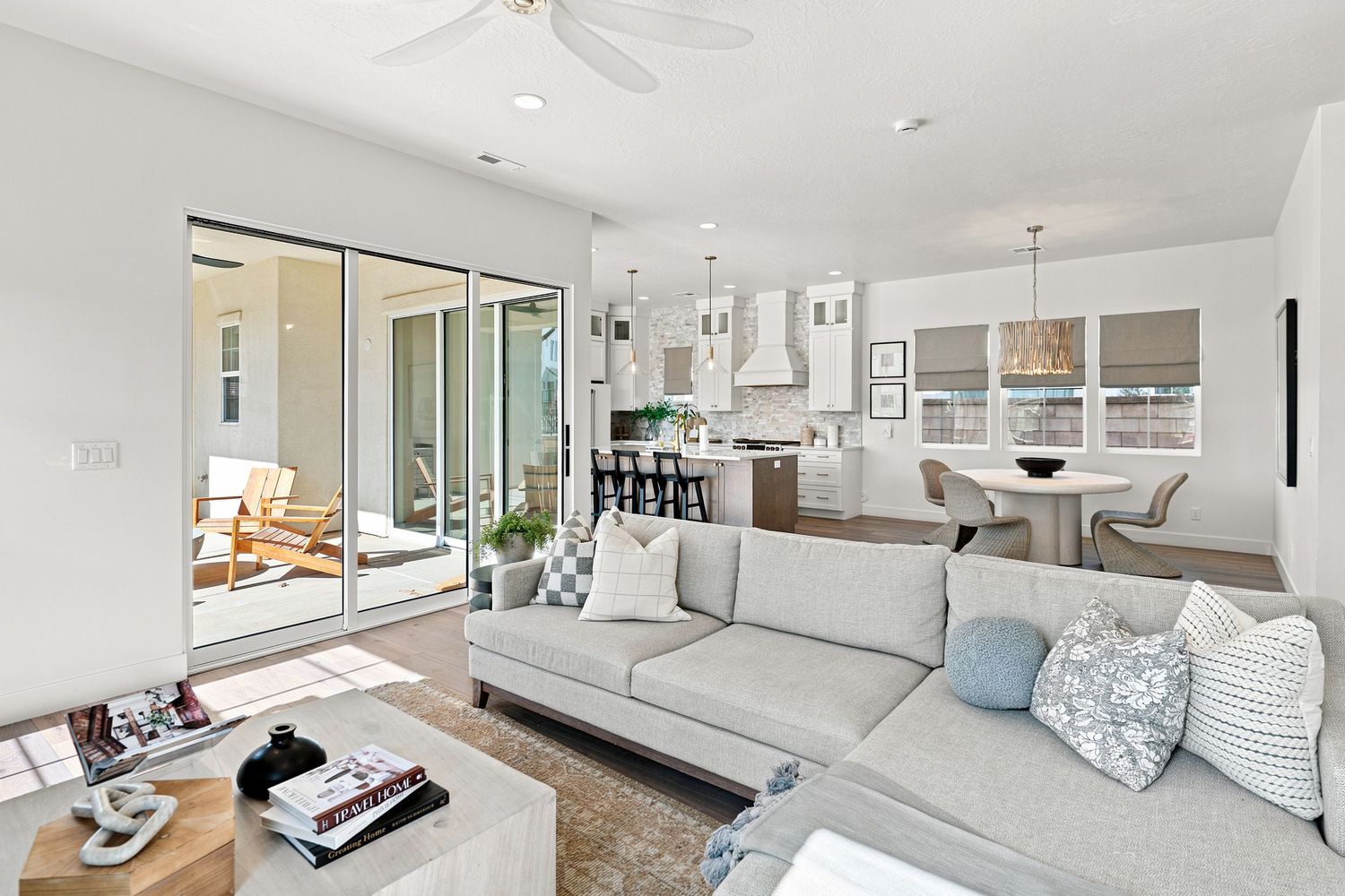 Bright open-plan living room with gray sectional sofa, sliding glass doors, and modern kitchen in background.
