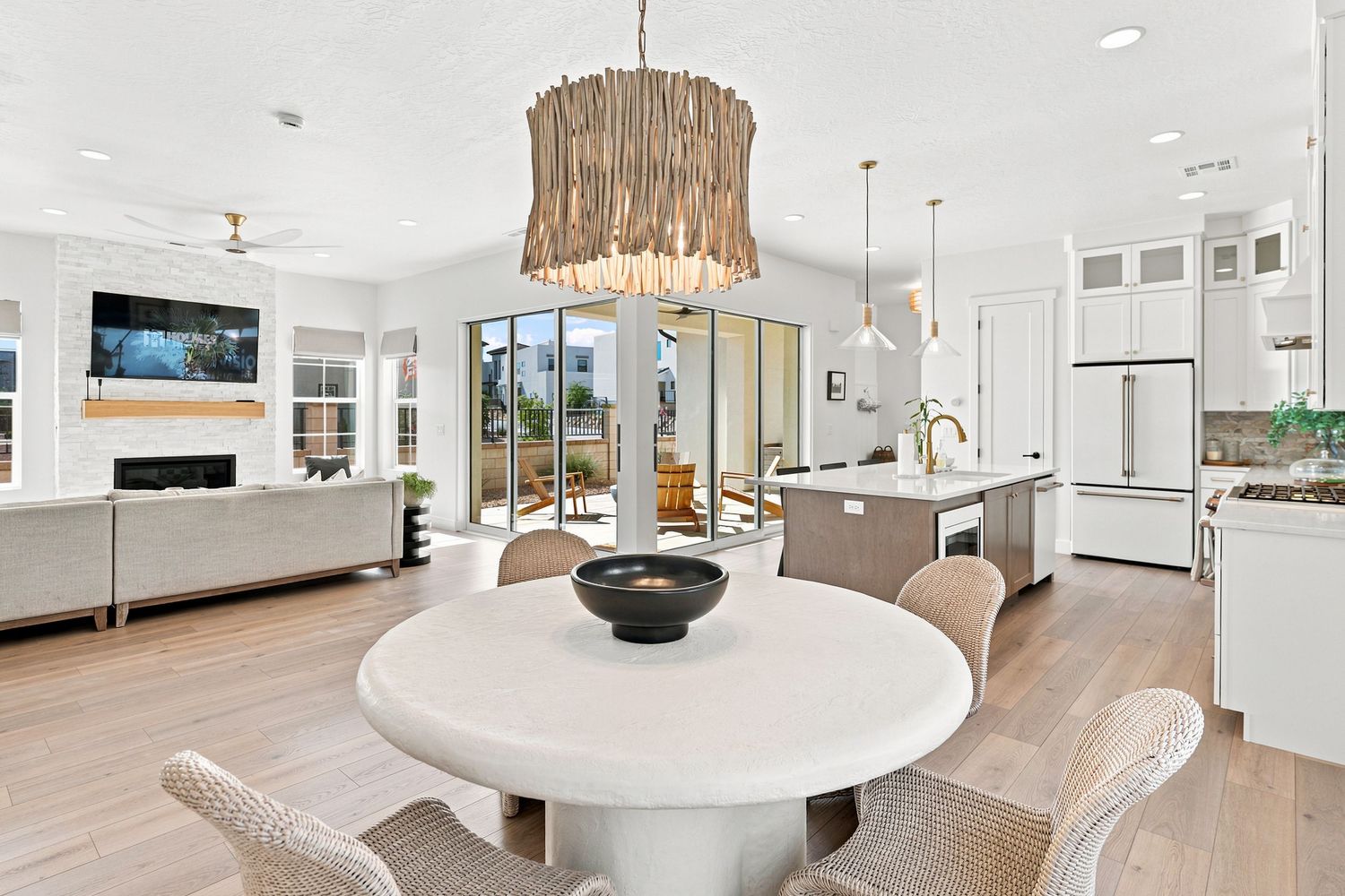 Open-concept dining area with round white table, driftwood chandelier, and modern kitchen in bright coastal home.